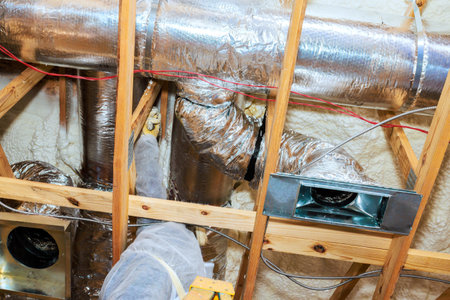 Workers are installing metal ducts in an attic, ensuring proper ventilation for new home.
