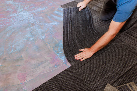 Worker carefully lays down carpet tiles on neat installation in new room