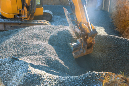 Yellow excavator digs into pile of gravel at construction site worker is managing equipment under...