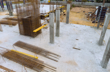 Steel rods lay on ground while concrete pillars stand firm at construction site for building...