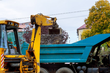 Construction machine uses its arm to load gravel into truck on worksite in city