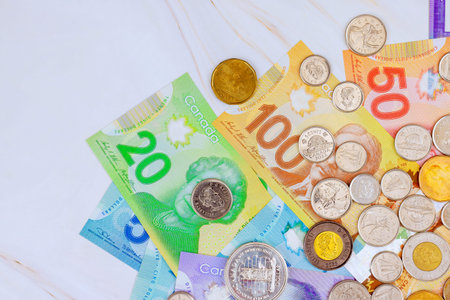 Several Canadian banknotes, coins are spread out on flat surface their different designs colors.