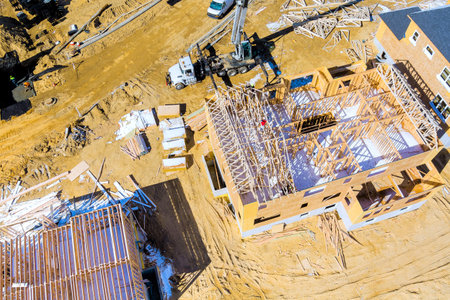 Workers use cranes to lift roofing joist for houses under construction in new development areaの写真素材
