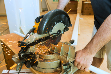 Contractor operates circular saw to cut through metal, creating sparks in busy workshop environment.