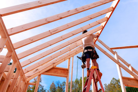 Worker stands on ladder to build roof frame with wooden beams at construction site