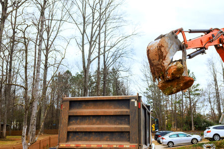 Workers use backhoe to load dirt rocks into dump truck at residential siteの写真素材