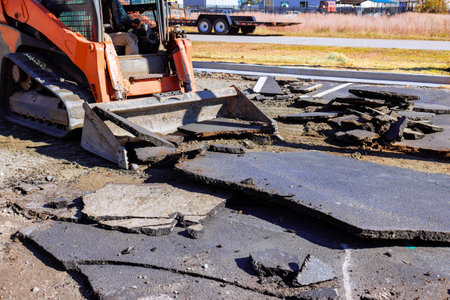 Construction work is ongoing as bulldozer clears broken asphalt, preparing area for repairs parking...