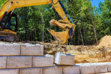 Construction work with an excavator moving heavy stone blocks under build sturdy retaining wall