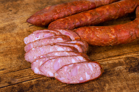 Sausage links are placed on wood with few slices showing inner texture highlighting preparation for...
