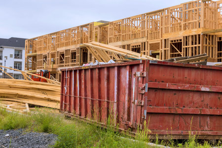 Building new residential building, wooden beams are stacked near red construction dumpster...