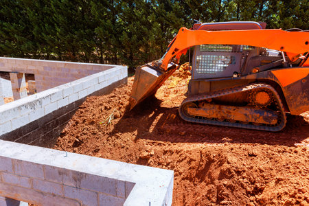 Small excavator works on construction site, moving dirt to create foundation.