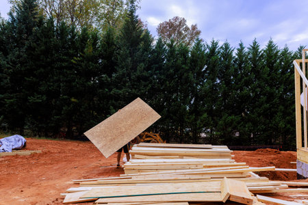 Framing worker carries wooden osb board at construction site with pilesの写真素材