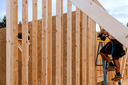 Construction worker uses tools on ladder to assemble wooden frame of building under work continues