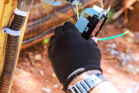 Electrician is working with electrical wires at control box while standing outside