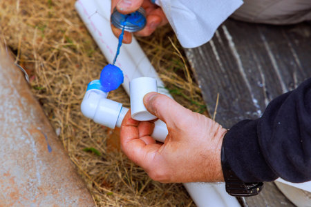 Worker uses glue to attach two pieces of plastic pipe while crouched on ground