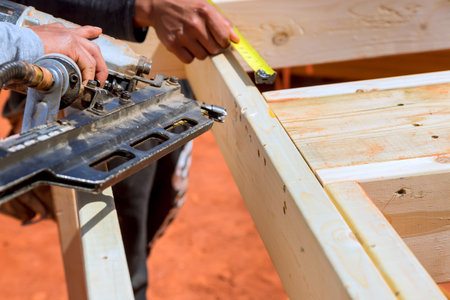 Worker cuts wood using saw while measuring with tape in construction site