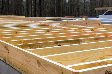 Workers lay out wooden beams at construction site in forest with tools nearby.