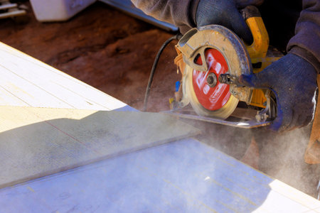 Carpenter operates circular hand saw to cut through wood on construction site dust, debris fly.