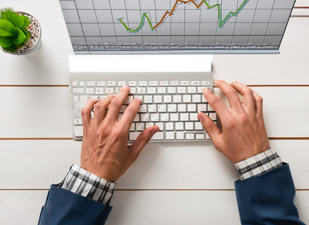 top view of businessman working with laptop at desk with financial chart on screenの素材