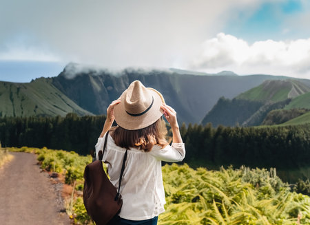 Young woman traveler with hat and backpack looking at beautiful view of the mountains.の素材