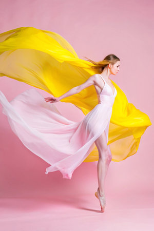 Young beautiful ballerina dancing with yellow and pink cloth on pink backgroundの素材