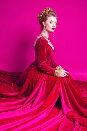 Portrait of a beautiful young woman in red dress on a pink backgroundの素材