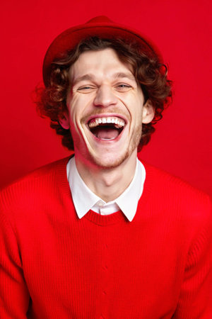 Portrait of a happy young man laughing against a red background.の素材