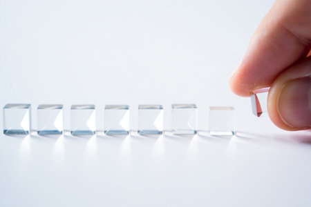 Glass cubes arrangement. Hand placing cube. White background. Soft studio lighting. Transparent design.の素材