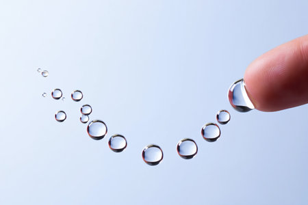 Science concept of finger touching floating water droplets on light blue background.の素材