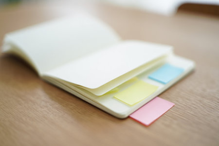 Open notebook with blank pages. Sticky notes on wood table. Minimalist workspace.の素材