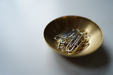 Brass bowl of paper clips. Office workspace organization aesthetic concept.の素材