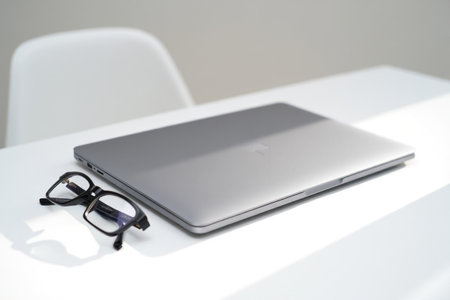 Laptop and eyeglasses on white desk. Technology business workspace. Minimalist style.の素材