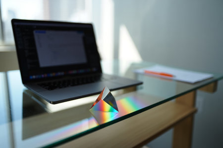Prism on desk. Rainbow light. Refraction experiment. Creative workspace ambiance.の素材