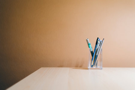 Collection of pens and pencils in glass cup on desk. Office suppliesの素材