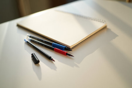 Open notebook. Pens on light surface workspace. Creativity, focused writing.の素材