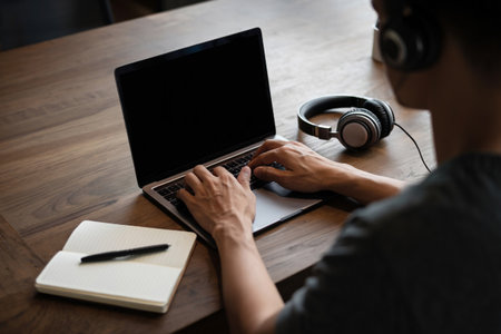 Typing on laptop with headphones. Notepad on wood desk technology.の素材