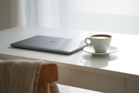 Laptop and coffee on white desk. Minimalist work environment setup.の素材