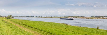 Clouded river landscape with a transport ship on a river in the Netherlandsの写真素材