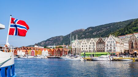 Bergen, Norway, Scandinavia - July 30, 2019: Norwegian flag with the port of Bergen and view on the historical buildings of Bryggen in Bergen, Norwayのeditorial素材