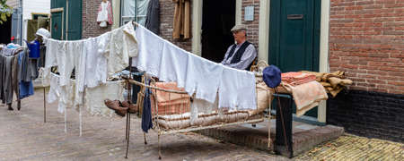 Enkhuizen, The Netherlands - July 7, 2021: Man in traditional cloths in front of his outdoor cloth shop in the streets of Zuiderzee museum in Enkhuizen North-Holland in The Netherlandsのeditorial素材