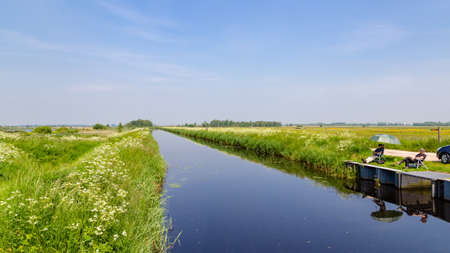 Leek, The Netherlands - June 4, 2021: Fishermen along cnala in nature reserve De Onlanden with pond and wild blooming flowers near Groningen city The Netherlandsのeditorial素材