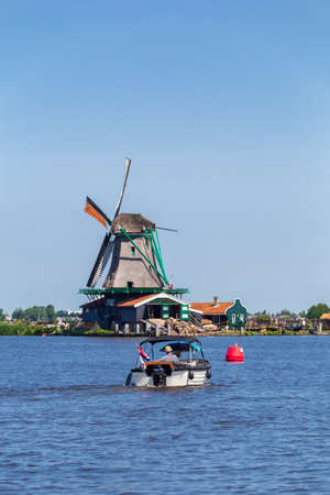 Zaanstad, The Netherlands - July 18, 2021: Man in little boat sailing towards colorful old windmill in Zaanse Schans Village in Zaanstad North Holland The Netherlandsのeditorial素材