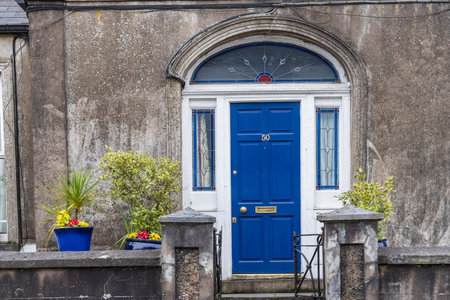 Ornamental front yard with blooming flower pots surrounded by walls and old house with blue door along Lee river in Cork Munster province in Ireland Europeの写真素材
