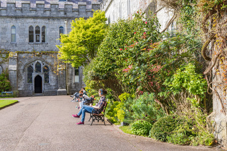 Cork, Ireland - April 17, 2023: Stduents on bench in front of main building with facade garden of University College of Cork Munster province in Ireland Europeのeditorial素材