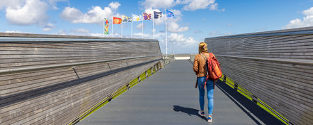Delfzijl, The Netherlands - August 8, 2023: Female tourist with backpack crossing the bridge to viewing platform and promenade along the beach of Delfzijl in Groningen province in The Netherlandsのeditorial素材