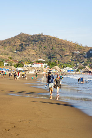 San Juan del Sur, Nicaragua - March 23, 2024: Tourist couple walking along the beach of San Juan del Sur coastal town on the Pacific Ocean in the Rivas department in southwest Nicaragua.のeditorial素材