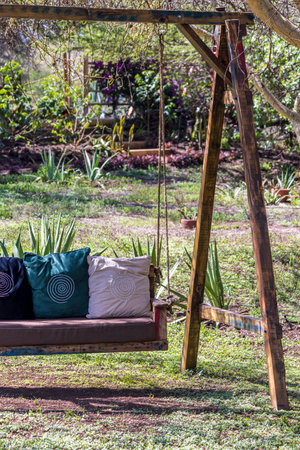 Enjoying the beautiful weather on relaxing swing bench with pillows in a green gardenの写真素材
