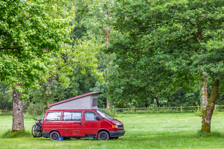 Cozy little red camper with lifting roof parked at meadow between treesの写真素材