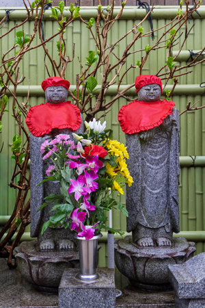 Two Buddha statue with red clothing and flowers at entrance of Saikoji temple in Yanaka subsurb in Tokyo, Japan.の写真素材