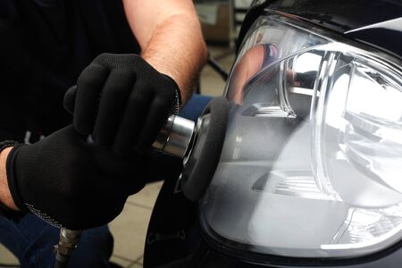 The worker polishes optics of headlights of the car with the electric tool. Close upの写真素材